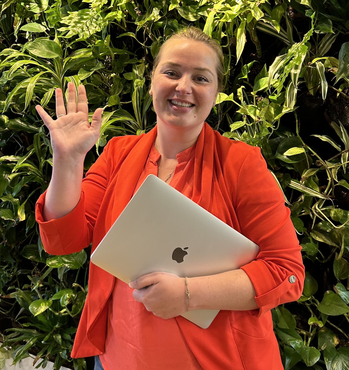 Anne Mooiwerk staat met een laptop in haar hand voor een wand met planten.